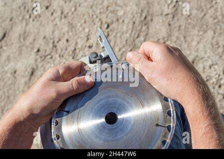 a man removes the plastic protection from the saw blade teeth on a circular miter saw for installation and replacement. Stock Photo