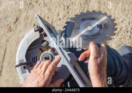 a man replaces a saw blade on a circular miter saw for woodworking. Stock Photo
