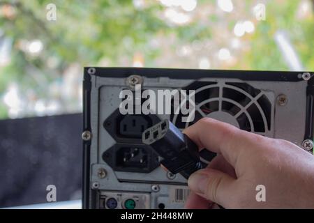 Power supply PSU of a computer with turned off button and holding the power cable for the pc with a hand. Stock Photo