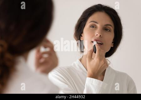 Woman in bathrobe applying lipstick on lips Stock Photo