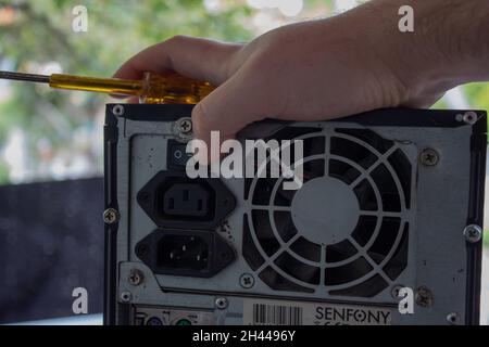Pressing the on, off button on the power supply of a computer with a finger while holding a yellow screwdriver. Stock Photo