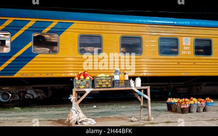 Stall and buckets with apples, drinking water beside the 3rd class train car painted in national colors of Kazakshtan. On a train stop in Turkistan Stock Photo