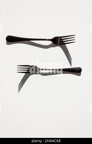 Two forks with sharp shadows of sun on a white background. Menu design concept. Flat lay. Copy space. Stock Photo