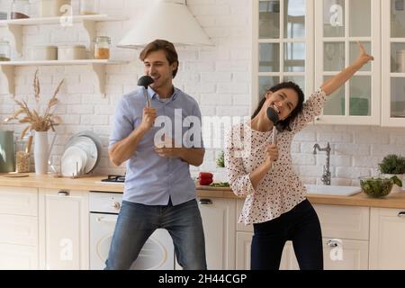 Lively attractive young couple singing dancing in kitchen Stock Photo