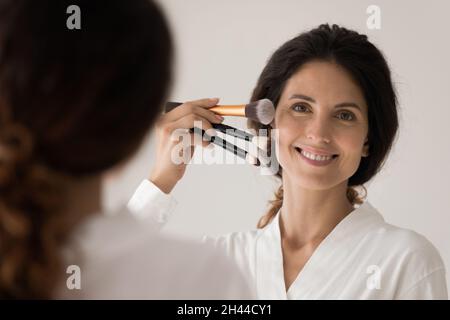 Woman holds near face kit of three different makeup brushes Stock Photo