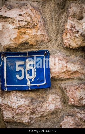 Number 55 plaque on a dirty old house wall. Stock Photo