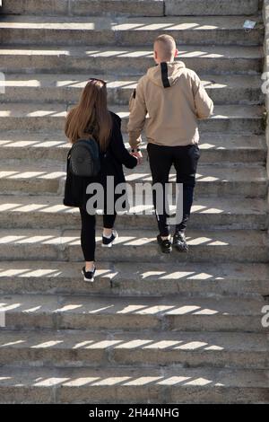 Two People Getting Steps In Young couple going up the stairs together, hand in hand, from behind ...