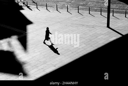 Shadow silhouette of a woman walking city street sidewalk square, in black and white from above with architectural shades Stock Photo