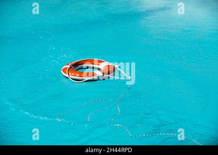 Lifebelt on sea or pool. Orange inflatable ring floating in blue water. Life buoy for protect and safety drowning. Stock Photo