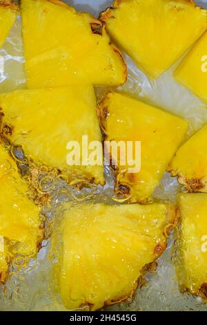 Pineapple close-up in liquid with bubbles. Slices of ripe pineapple in water. Close-up fresh slices of yellow pineapple on white background. Vertical Stock Photo