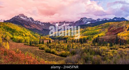 A colorful valley with the East Fork of Dallas Creek with dramatic Fall colors below Mount Sneffels and moody sunset clouds in the San Juan Mountains.