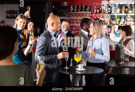 Cheerful middle aged woman with male colleague enjoying office party in bar, talking and toasting with drinks Stock Photo