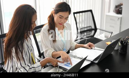 Two of professional business employees analysing and checking business data report together in the meeting room. Stock Photo