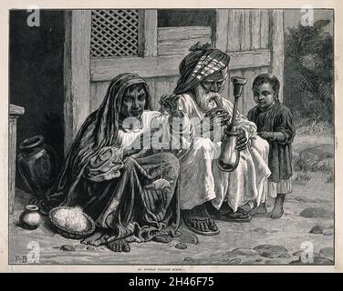 An old Afghan man sits with a woman and child on the ground smoking a hooka. Wood-engraving after F. Dadd. Stock Photo