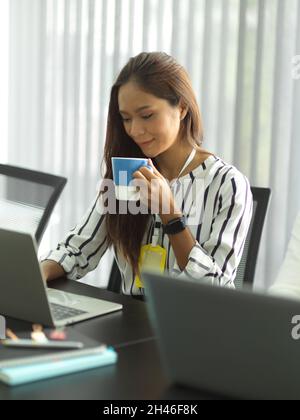 Portrait of beautiful young business workers drinking afternoon coffee while working on laptop computer. relax, break, rest. Stock Photo