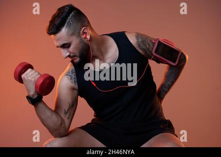 Handsome strong young man doing exercise with heavy dumbbell to pump up biceps muscles Stock Photo