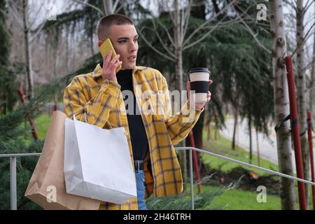 Young man with makeup on speak on the smartphone with shopping bags. Stock Photo