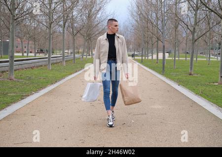 Young man wearing make up walking with shopping bags and listening music. Stock Photo