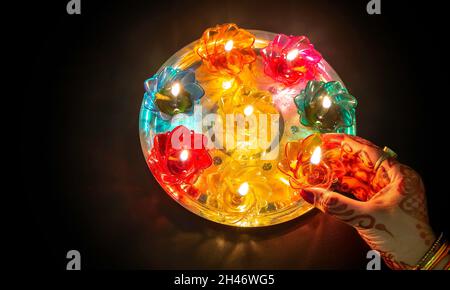 Woman hand wearing mehndi and bangles in close up holding a Diwali Diya lamp in dark background Stock Photo