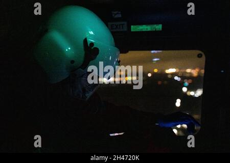 PRODUCTION - 11 October 2021, Baden-Wuerttemberg, Stuttgart: Emergency physician Dr. Christoph Herzog monitors his patient's vital signs on a display during the flight to a hospital, while his helmet is illuminated green by the control panel above him and the lights of the city can be seen through the window in the background. The rescue helicopter Christoph 54 is the only one in Baden-Württemberg that also has night flying capabilities. The night crew with the two pilots takes over the flying intensive care unit from 6.30 p.m. in the evening until 7 a.m. the following morning. It is stationed Stock Photo