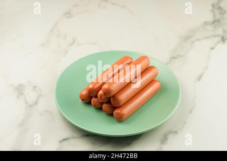 a stack of raw sausages on a green ceramic plate and a white dark table. cloceup Stock Photo