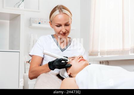 Professinal beautician surgeon using a laser device for removing mole. Removal of birthmark from female face. Electrocoagulation and laser cosmelotogy Stock Photo