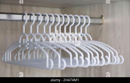 Silver horizontal metal rail with group of white empty plastic clothe hangers in row in wooden closet. Organize storage boutique store accessory, disc Stock Photo