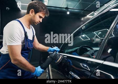 Repairman with orbital polisher fixing scratches on car side Stock Photo