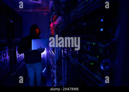 Cybercrook typing on notebook in server room Stock Photo