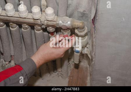 Professional service and repair of heating systems Concept. Specialist opens the water tap of the floor heating system. An adult male performs start-u Stock Photo