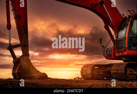 Backhoe parked at construction site after digging soil. Bulldozer on sunset sky and clouds background. Digger after work. Earth moving machine Stock Photo
