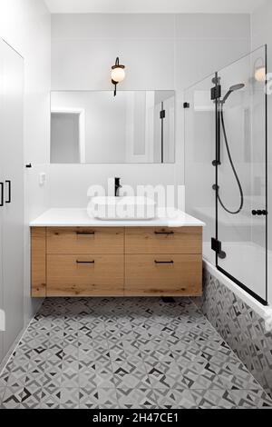 Bathroom, brown wooden cabinet, illuminated light fixture and varied floor tiles Stock Photo