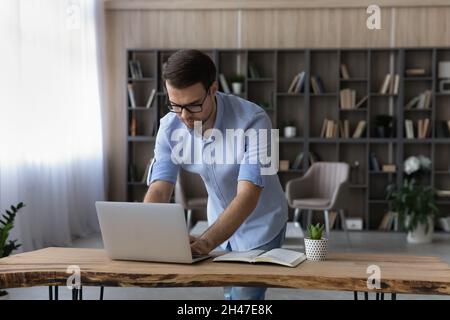 Concentrated young businessman working on computer, standing at table. Stock Photo