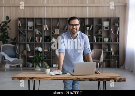 Portrait of happy young handsome businessman standing at table. Stock Photo
