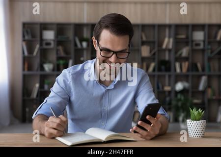 Happy young business man writing notes using cellphone. Stock Photo