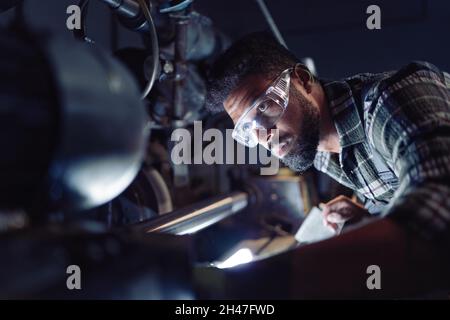 Close up of young concentrated african american industrial man working on cutter indoors in metal workshop. Stock Photo