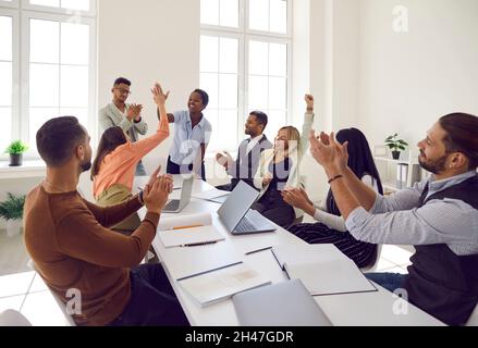 Happy diverse business team sitting at office table, celebrating successful deal and applauding Stock Photo