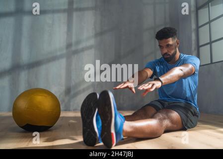 Young sportsman sitting on floor and doing stretching exercise indoors, workout training concept. Stock Photo