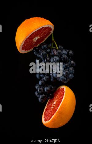 Dark blue grape with red grapefruit on black background Stock Photo