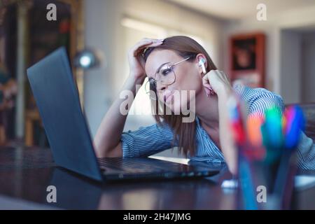 Young Caucasian woman with hands free device listening music at laptop in home office Stock Photo