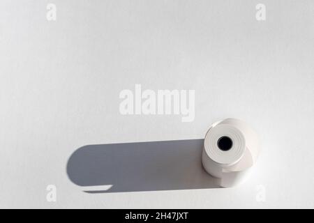 Roll of cassette paper tape with shadow on white paper, copy space. Roll of cash register tape, slip receipt paper roll, isolated on white background Stock Photo