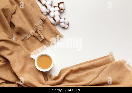 Beige cashmere scarf with a cup of coffee and a sprig of cotton on a light gray background. Flat lay top view copy space. Autumn winter coziness conce Stock Photo