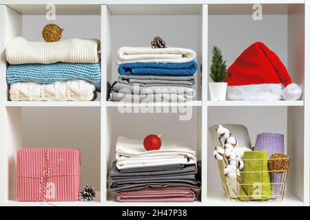 Organization of storage. Bed linen, towels, sheets, knitted sweaters on the shelves decorated for the celebration of Christmas and New Year. Stock Photo