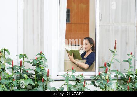 Middle-aged woman enjoying resting on sofa and reading interesting book Stock Photo