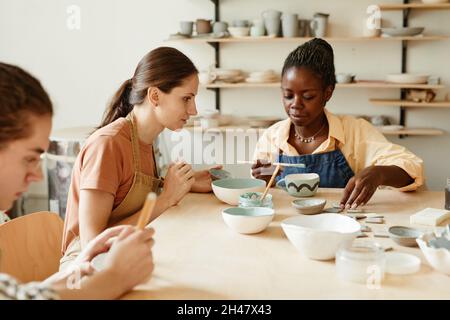 Side view portrait of young woman enjoying pottery workshop in cozy studio, copy space