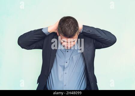 Businessman with stiff neck or tension headache holding his hands behind his head while grimacing in pain on a blue background. medical concept Stock Photo