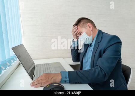 Young male employee wearing hygiene mask feels headache and rise hand to touch her head. Idea for healthcare in office. the businessman is sick of cov Stock Photo