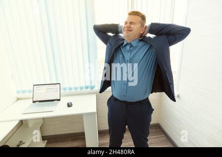 Businessman stretching out at desk with laptop. Manager make deep breath of fresh air, relaxed after finishing work. Office worker doing relaxing exer Stock Photo