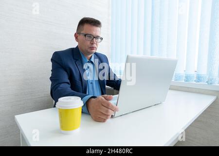 Businessman sitting at office desk having a coffee break, he is holding a mug and a digital tablet Stock Photo