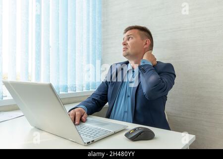 Businessman with neck pain after long hours at work. health problems from sedentary work. a man in a suit is holding on to a sore neck Stock Photo